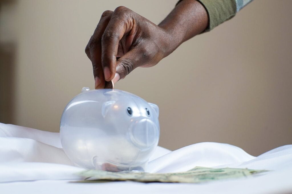 Person Putting Coin in a Piggy Bank | Saccos and Savings Culture